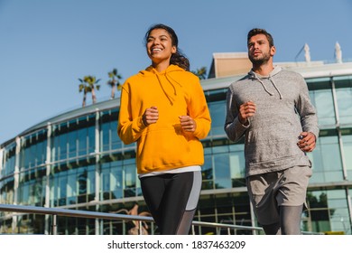 Happy Young Mixed Race Couple Jogging In Sporty Outfit In Urban Area