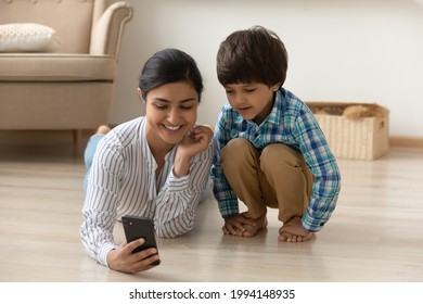 Happy Young Mixed Race Ethnicity Mom And Little Son Look At Smartphone Screen Talk Speak On Video Call. Smiling Indian Mother And Small Boy Child Use Cellphone Have Webcam Virtual Digital Event.