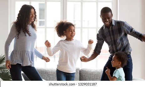 Happy Young Mixed Race Family Of Four Have Fun Together In Living Room, African American Mom And Dad Entertain With Little Kids, Dancing At Home, Black Parents Enjoy Spending Time With Small Children