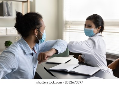 Happy young mixed race male patient and female gp doctor in facial protective masks touching elbows, starting or finishing checkup meeting in clinic, avoiding hand contact, covid prevention cocept. - Powered by Shutterstock