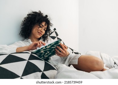 Happy Young Mixed Race Woman Relaxes Reading Journal Notes On Bed. Copy Space.