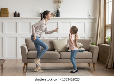 Happy Young Mom Baby Sitter Sister And Cute Funny Little Kid Daughter Laughing Dancing In Living Room Together, Cheerful Active Mother With Child Girl Having Fun Enjoy Moving To Music Playing At Home