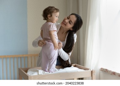 Happy young mom dressing cute toddler girl on baby changing table. Loving mother talking and caring of little child with tenderness, affection, enjoying motherhood, maternity leave. Childcare concept