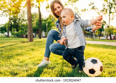 Happy young mom and her little son play soccer together outdoors in the park