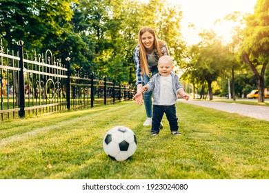 Happy Young Mom And Her Little Son Play Soccer Together Outdoors In The Park