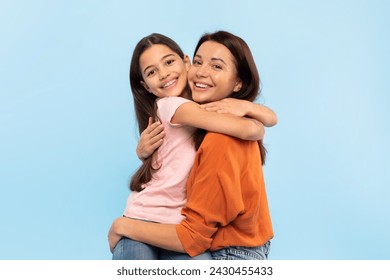 Happy Young Mom Hugging Her Little Daughter Smiling To Camera Over Blue Background In Studio, Loving Family Of Two Mom And Preteen Kid Girl Posing Together And Bonding - Powered by Shutterstock