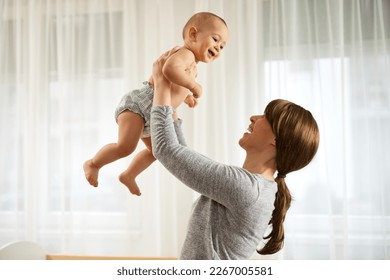 Happy young mom lifting her adorable little newborn baby boy in the air - Powered by Shutterstock