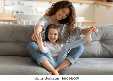 Happy young mom sit rest on couch in kitchen feel playful have fun with cute little girl child, smiling mother play with funny small daughter relax enjoying family weekend at home together