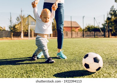 Happy young mom with son play soccer on the field, outdoors