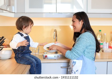 Happy Young Mother Cleaning Dishes With Her Kid At Kitchen Home. Asian Woman Teaching Her Child With Housework.