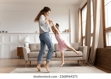 Happy young mother dancing swirling with excited little preschooler daughter relaxing together in living room, overjoyed millennial mom or nanny have fun with small girl child playing at home - Powered by Shutterstock