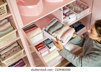 Happy young mother enjoying tidying up at female child wardrobe closet neatly folded clothes in plastic case box for comfortable vertical storage. Modern female cleanup kids cupboard Konmari method