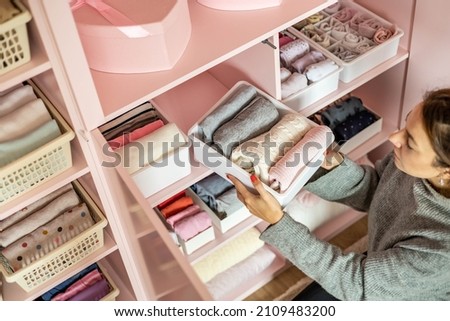Happy young mother enjoying tidying up at female child wardrobe closet neatly folded clothes in plastic case box for comfortable vertical storage. Modern female cleanup kids cupboard Konmari method