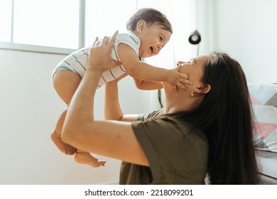 Happy young mother enjoying time with her adorable toddler son at home, lifting him in the air, playing with kid boy in living room - Powered by Shutterstock