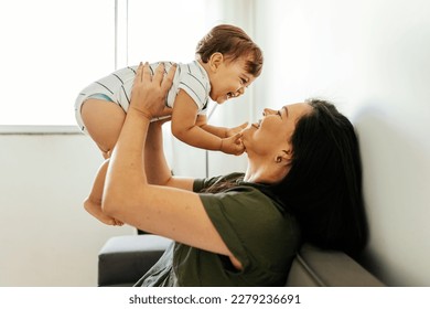 Happy young mother enjoying time with her adorable toddler son at home, lifting him in the air, playing with kid boy in living room - Powered by Shutterstock