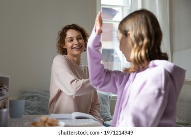 Happy young mother giving high five to smiling adorable little teen kid daughter, finishing learning together at home, preparing for school exams or doing homework, enjoying homeschooling, supporting.