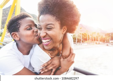 Happy young mother having fun with her child in summer sunny day - Son kissing his mum outdoor with back sun light - Family lifestyle, motherhood, love and tender moments concept - Focus on woman face
