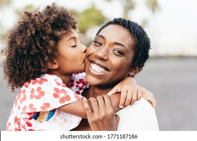 Fröhliche junge Mutter, die sich im Sommertag mit ihrem Kind amüsiert - Tochter küsst ihre Mutter im Freien - Familienleben, Mutterschaft, Liebe und zarte Momente - Fokus auf das Gesicht der Frau