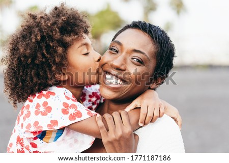 Happy young mother having fun with her child in summer day - Daughter kissing her mum outdoor - Family lifestyle, motherhood, love and tender moments concept - Focus on woman face