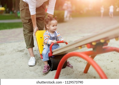 Happy Young Mother With Her Baby Girl Playing In Colorful Playground For Kids. Mom With Toddler Having Fun At Summer Park. Baby Play. Summer Family Leisure.