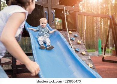 Happy young mother with her baby boy playing in colorful playground for kids. Mom with toddler having fun at summer park. Baby play in children's slide - Powered by Shutterstock