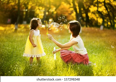 Happy young mother and her daughter blowing soap bubbles in autumn
