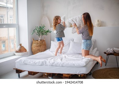 Happy young mother with her little girl at home playing on the bed with pillows, short brunette hair, the same clothes, striped T-shirts. - Shutterstock ID 1942414708