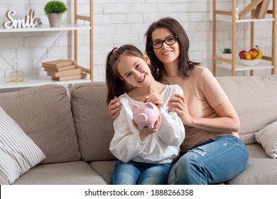 Happy Young Mother And Her Teen Daughter Holding Piggybank, Sitting On Sofa At Home, Copy Space. Family Budget, Financial Education For Kids, Savings And Investments Concept