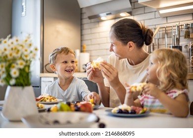 Happy young mother hugging little kids feeling love and tenderness sitting table with fresh homemade summer dessert waffles and fruits. Family weekend breakfast at home kitchen with positive emotion - Powered by Shutterstock