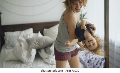Happy young mother and little cute daughter dancing near bed in bedroom at home