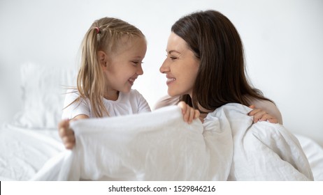 Happy Young Mother And Little Daughter Making Bed Together, Having Fun, Looking At Each Other Profile Close Up, Smiling Mum And Adorable Preschool Child Holding Blanket, Relaxing In Bedroom