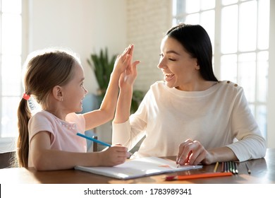 Happy young mother and little daughter giving high five close up, having fun, drawing colorful pencils, sitting at desk together, smiling mum and preschool girl enjoying leisure time at home - Powered by Shutterstock