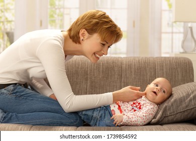 Happy Young Mother Playing With Little Baby Girl, Smiling. Side View.