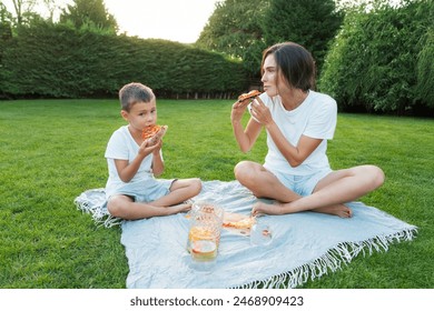 Happy Young mother and preschooler son having outdoor picnic dinner, eating pizza sitting on backyard Lawn on Sunny Day. Happy family time together. Active childhood. House in the suburbs in summer. - Powered by Shutterstock