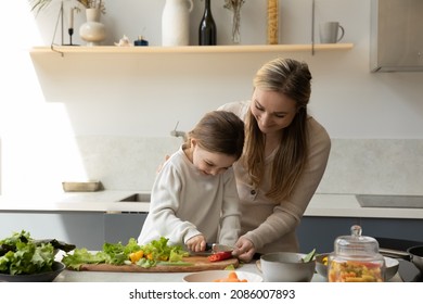 Happy young mother teaching little cute kid daughter preparing healthy food, chopping organic vegetables for fresh salad on wooden board together in modern kitchen, enjoying culinary hobby activity. - Powered by Shutterstock