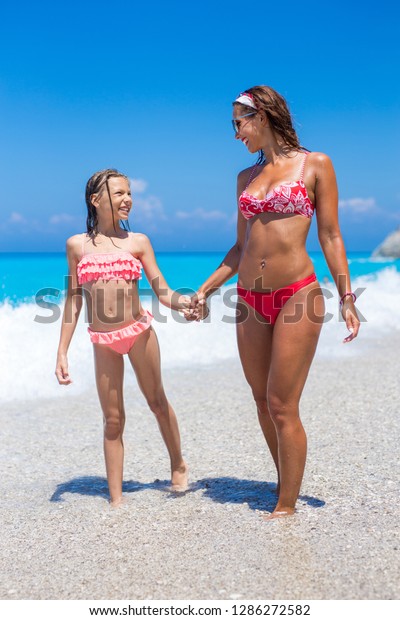 Happy young mother walking on the beach with her daughter while smiling.