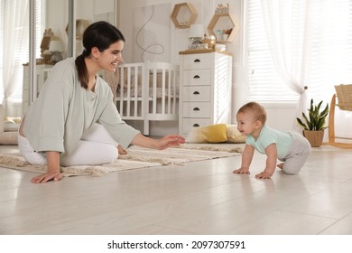 Happy young mother watching her cute baby crawl on floor at home