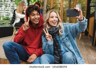 Happy young multhiethnic couple spending time together at the park, sitting, taking a selfie - Shutterstock ID 1416588194