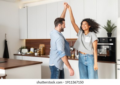 Happy Young Multi Ethnic Couple In Love Dancing And Holding Hands In The Kitchen. Joyful Boyfriend And Girlfriend Have A Fun At Home, Newlywed Moved In New Apartment