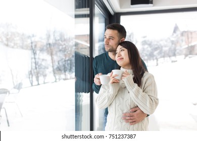 Happy Young Multiethnic Couple Enjoying Morning Coffee By The Window On Cold Winter Day At Home