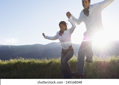 Happy young multiethnic couple jumping while holding hands in park - Powered by Shutterstock