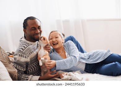 Happy young multiethnic couple relaxing and playing with dog at home - Powered by Shutterstock