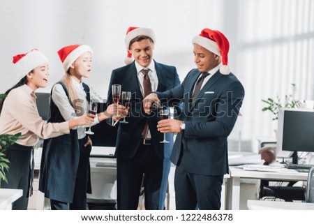 happy young multiethnic coworkers in santa hats celebrating xmas in office 