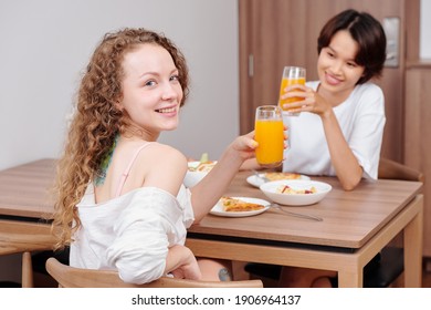 Happy Young Multi-ethnic Lesbian Couple Drinking Fresh Orange Juice When Having Dinner At Home