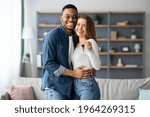 Happy young multiracial couple holding home keys and hugging, romantic millennial family, black man and white woman poising in living room after moving to new appartment, smiling at camera, free space