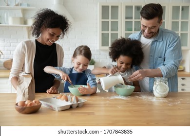 Happy young multiracial parents and little biracial daughters have fun baking in kitchen together, overjoyed family with cute small multiethnic children cooking in modern home preparing breakfast - Powered by Shutterstock