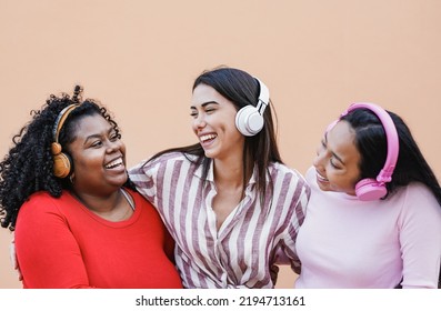 Happy young multiracial women hugging together while listening music playlist with wireless headphone