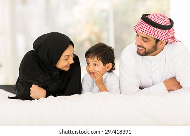 happy young muslim family of three lying on bed at home