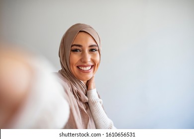 Happy young muslim woman take self portrait with handphone at home. Happy arab woman in hijab with mobile phone making selfie. Portrait of smiling girl, posing. - Shutterstock ID 1610656531