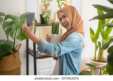A happy young muslim woman taking selfie with her plants and making video call at home  - Shutterstock ID 1973414576